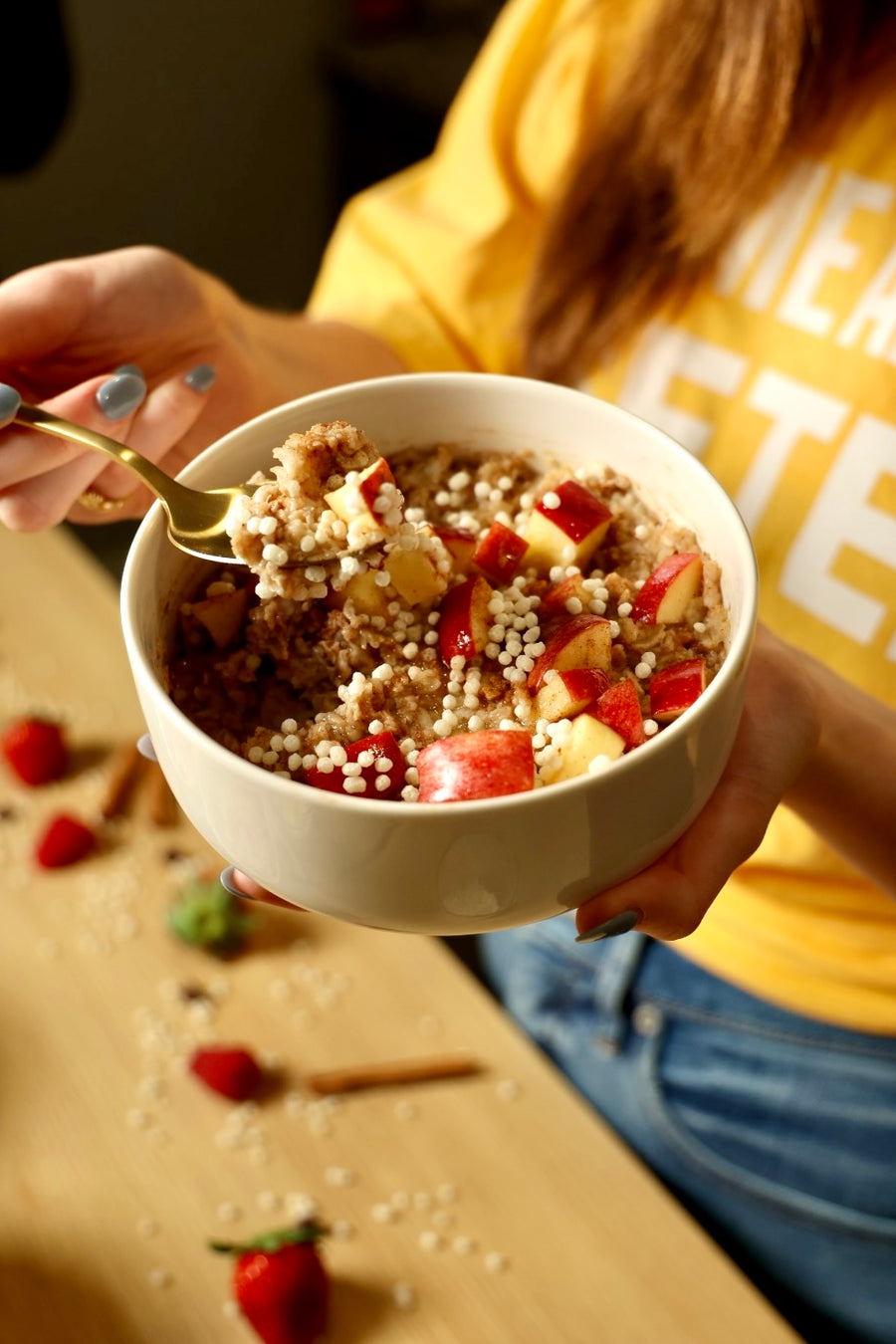 Person in a LIFTER t-shirt eating a bowl of oatmeal with apple, cinnamon, strawberries, and LIFTER Crispies