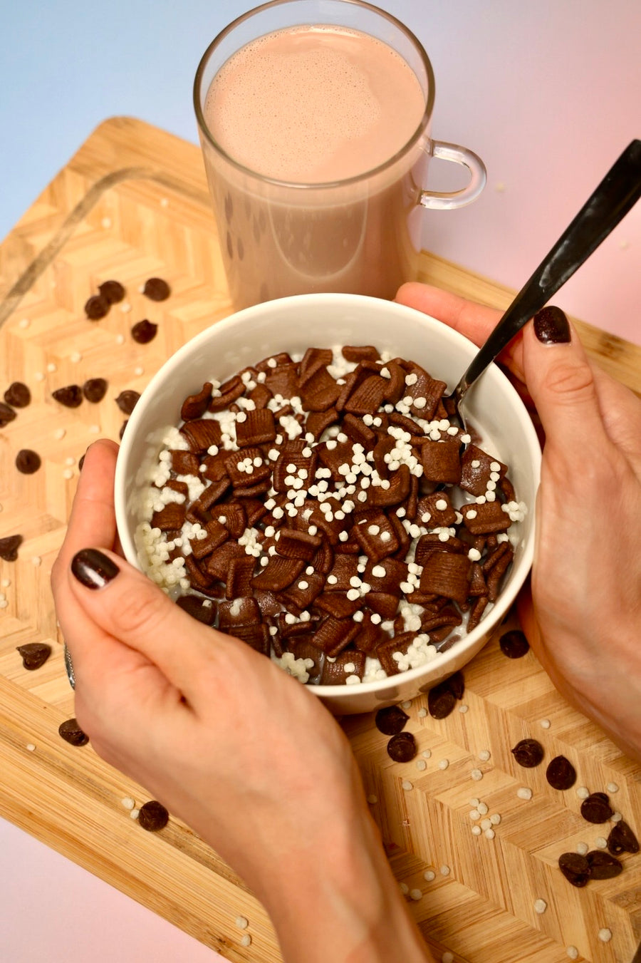 Hands holding a bowl of chocolate pieces topped with LIFTER Crispies next to a glass of chocolate protein shake